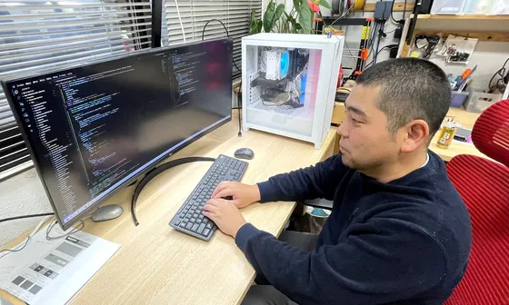 横長のモニタに表示したコードに向かって、技術者がキーボードを打っている様子。