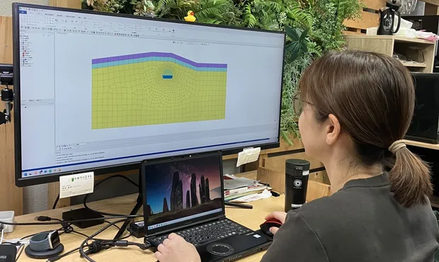モニタに表示した地盤の解析モデルを見ながら、パソコンで作業している職員